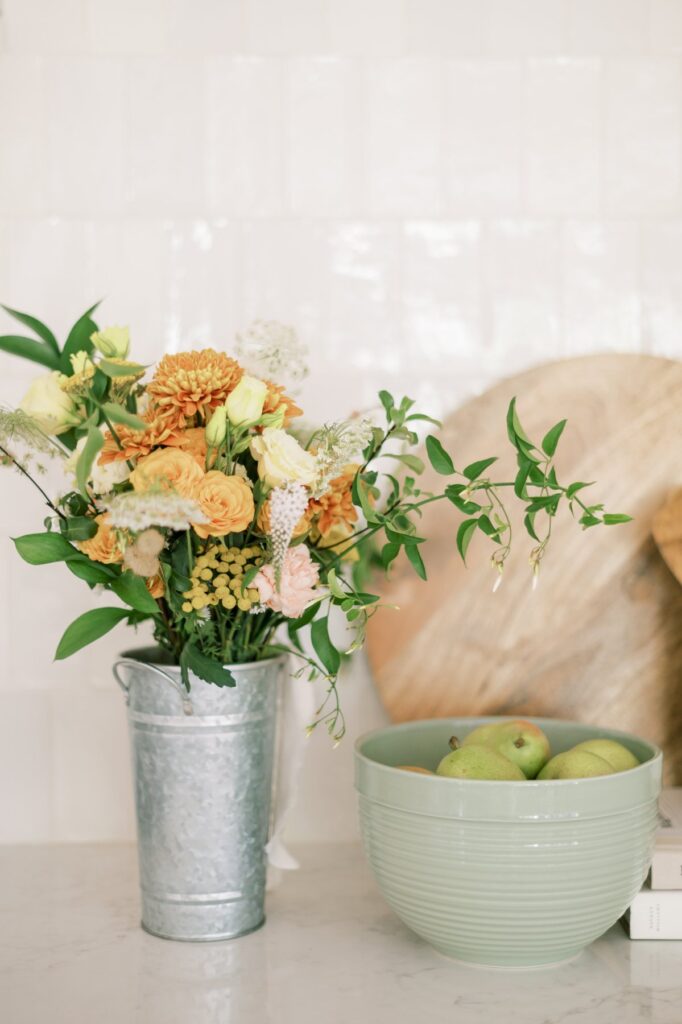 Fresh yellow and white flowers in a metal vase on a kitchen countertop.